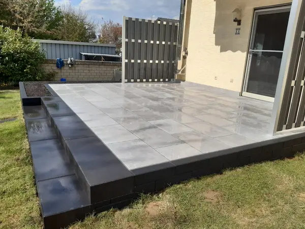 Terrasse mit hellen Platten, dunklem Sockel und Stufe zum Garten
