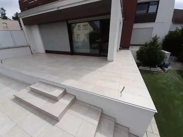 Erhöhte Terrasse mit hellen Feinsteinzeugplatten und breiter Treppe zum Rasen