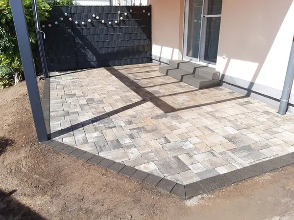 Gepflasterte Terrasse mit Sichtschutzzaun und Stufen zur Terrassentür